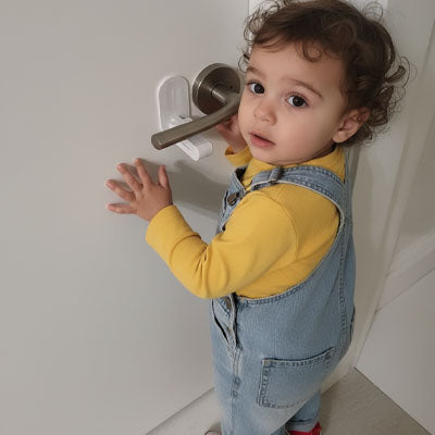 bloque porte bebe blanc bébé jaune gilet essaie ouvrir porte poignée levier