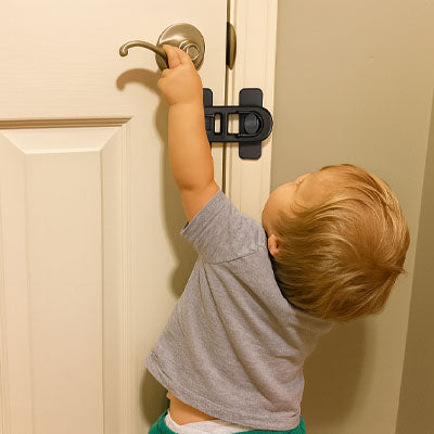 bloque porte bebe noir enfant gris debout dos essaie ouvrir porte blanche cadre